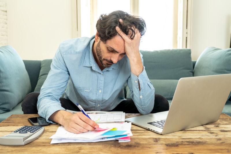 年轻的愤怒和担心的人工作与笔记本电脑在家里看账单和支付账单在家庭金融概念